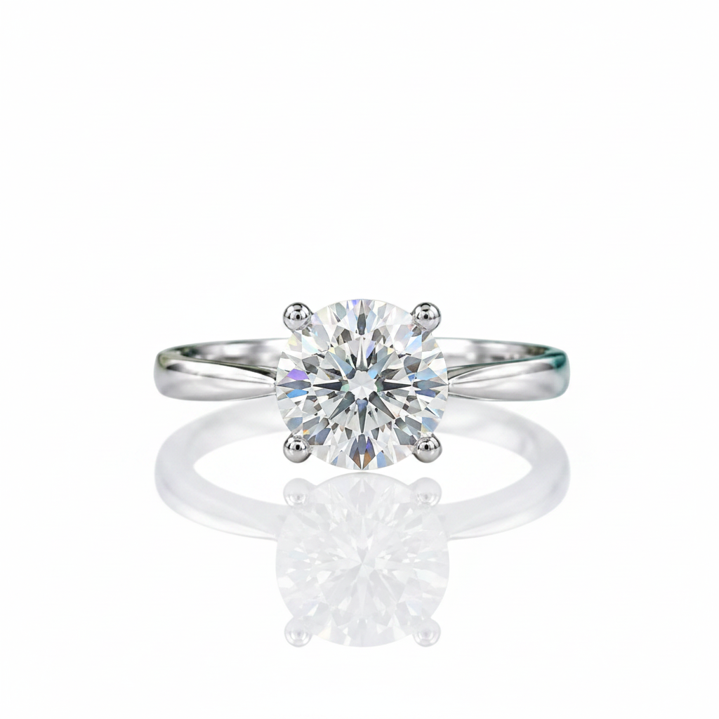 A classic solitaire engagement ring featuring a round brilliant-cut diamond set in a polished white gold or platinum band, displayed on a reflective white surface.