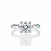 A classic solitaire engagement ring featuring a round brilliant-cut diamond set in a polished white gold or platinum band, displayed on a reflective white surface.