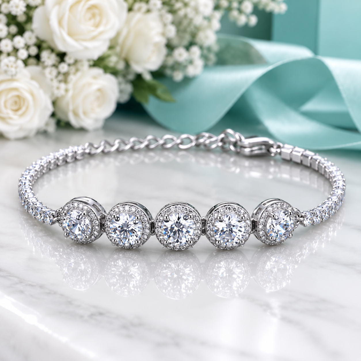 A silver-toned bracelet with five round-cut clear gemstones in halo settings, displayed on a white marble surface with white roses, baby's breath, and a light blue ribbon in the background.