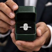 An oval-cut diamond engagement ring with a radiant-cut center stone in a four-prong setting, featuring a pavé-set band in white metal, shown on a clean white background with a soft reflection below.