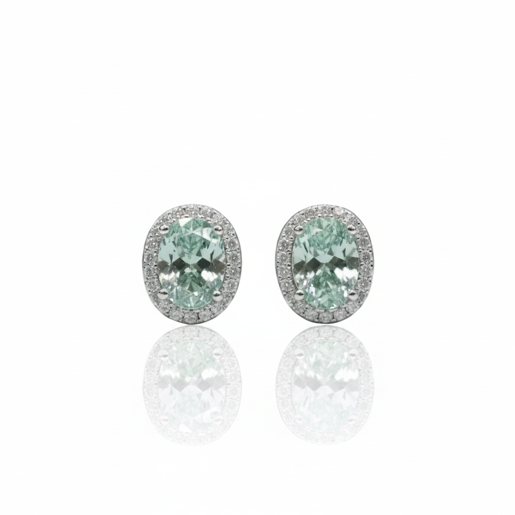 A pair of oval stud earrings featuring light green marquise-cut center stones surrounded by a halo of small clear stones in a silver-toned setting, displayed on a reflective white surface.