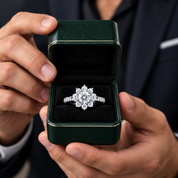 A close-up of a man holding an open dark green ring box with a silver-toned diamond ring featuring a floral snowflake design on a black velvet interior.