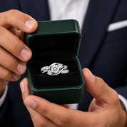 A close-up lifestyle shot of a man holding an open dark green ring box with a silver and diamond engagement ring displayed inside, with his face blurred in the background.