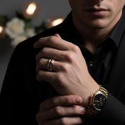 Man wearing a gold watch and ring, with a blurred background of flowers and lights.