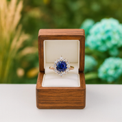 Blue gemstone ring in a wooden box with a blurred green floral background