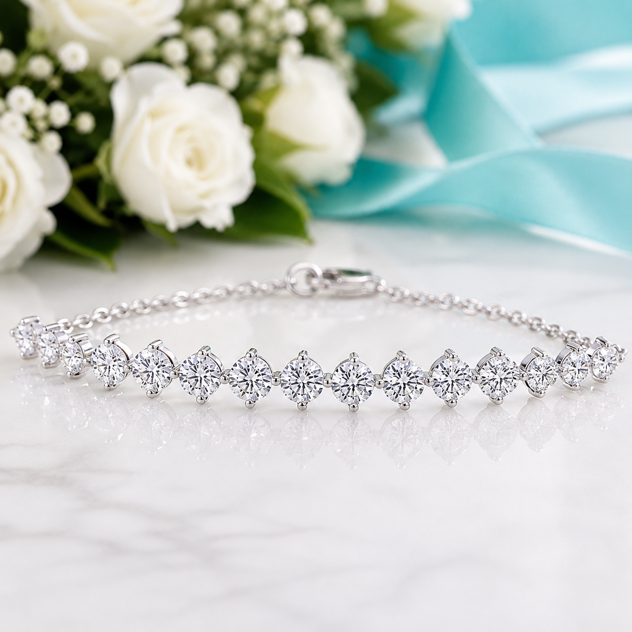 A silver tennis bracelet with clear gemstones arranged in a repeating floral pattern, resting on a white marble surface with white roses and a light blue ribbon in the background.