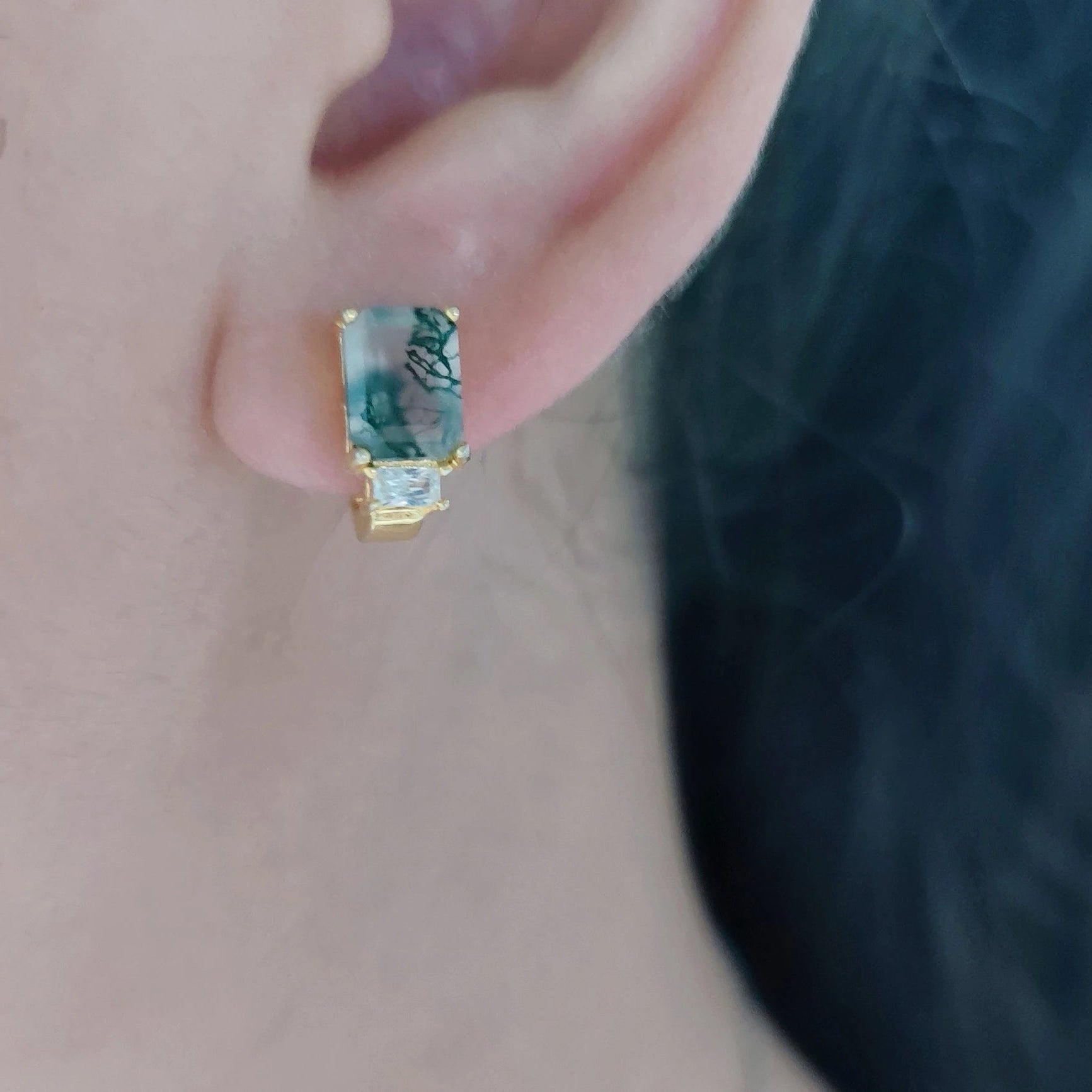 Close-up of a gold earring with a blue gemstone on an ear.