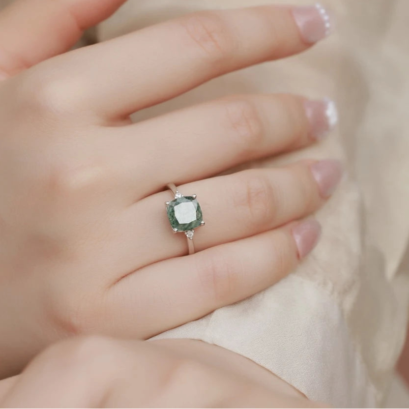 Close-up of a hand wearing a green gemstone ring with a blurred background