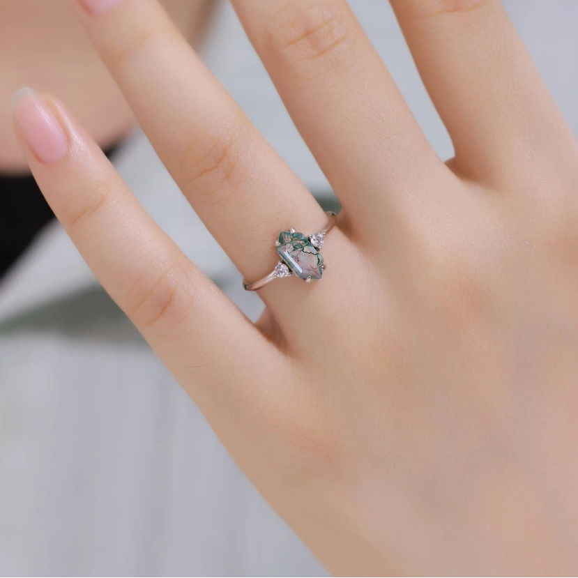 Close-up of a hand wearing a ring with a green gemstone, blurred background