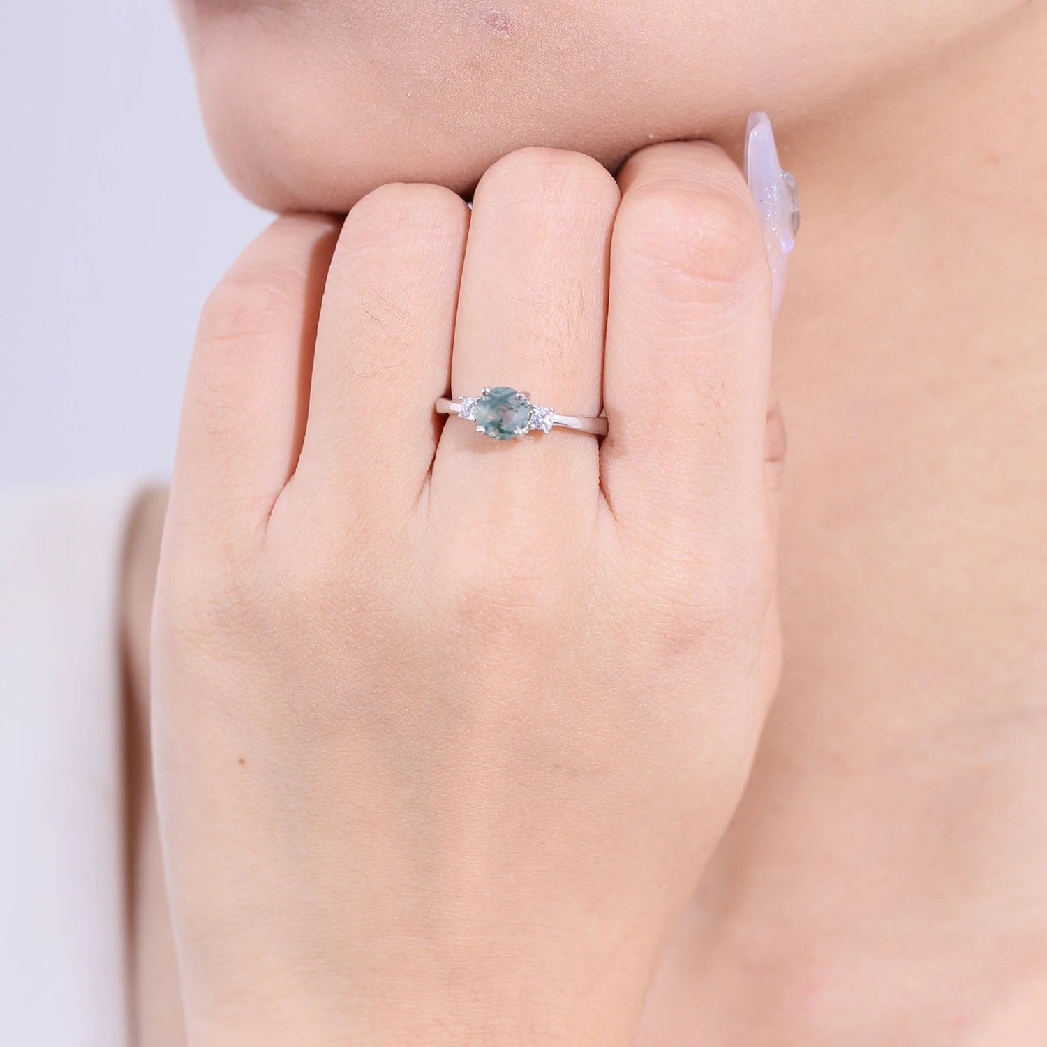 Close-up of a hand wearing a ring with a green gemstone on a neutral background