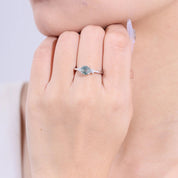 Close-up of a hand wearing a ring with a green gemstone on a neutral background