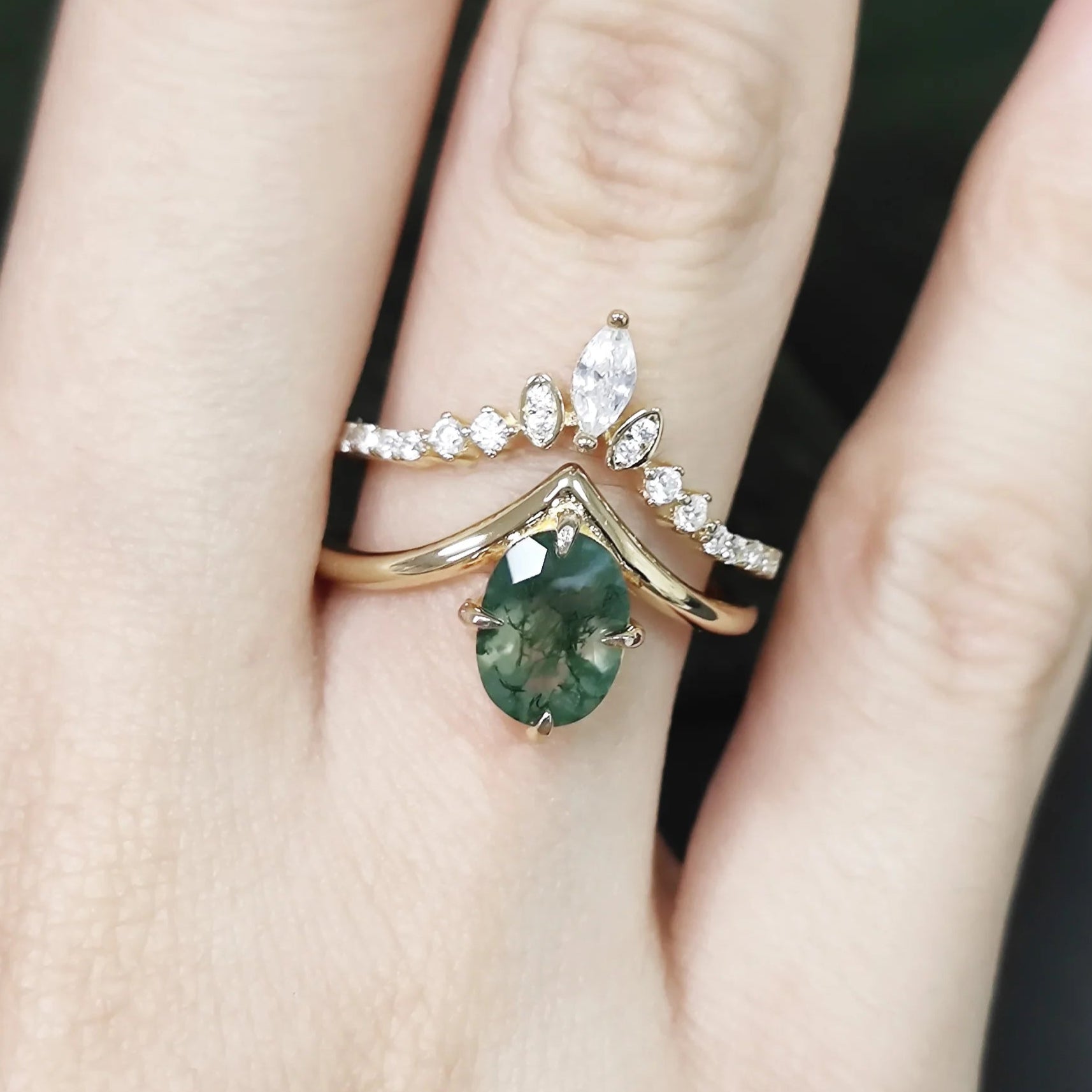 Close-up of a hand wearing two gold rings with green gemstones and diamond accents.