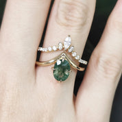 Close-up of a hand wearing two gold rings with green gemstones and diamond accents.