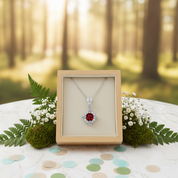 Diamond necklace with red gemstone in a wooden box on a table with a forest background
