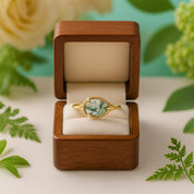 Gold ring with a green gemstone in a wooden box against a floral background
