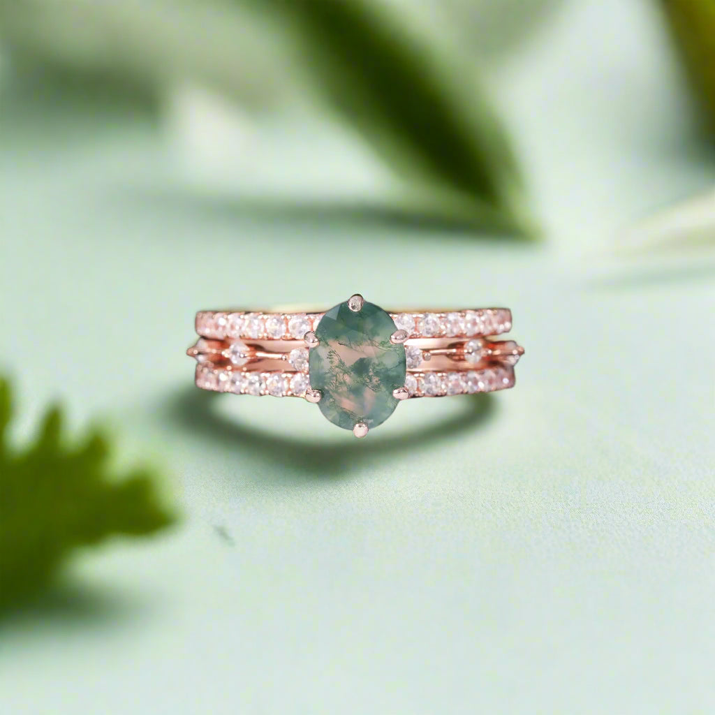 Stack of rose gold rings with a green gemstone on a dark surface