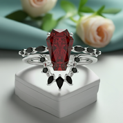 Elegant ring with a red gemstone and black stones on a white box with flowers in the background