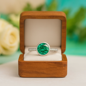 Emerald green gemstone ring in a wooden box with a blurred floral background