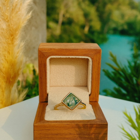 Gold ring with green gemstone in a wooden box against a natural background