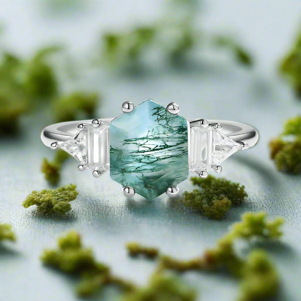 Silver ring with a green gemstone and clear diamonds on a white background