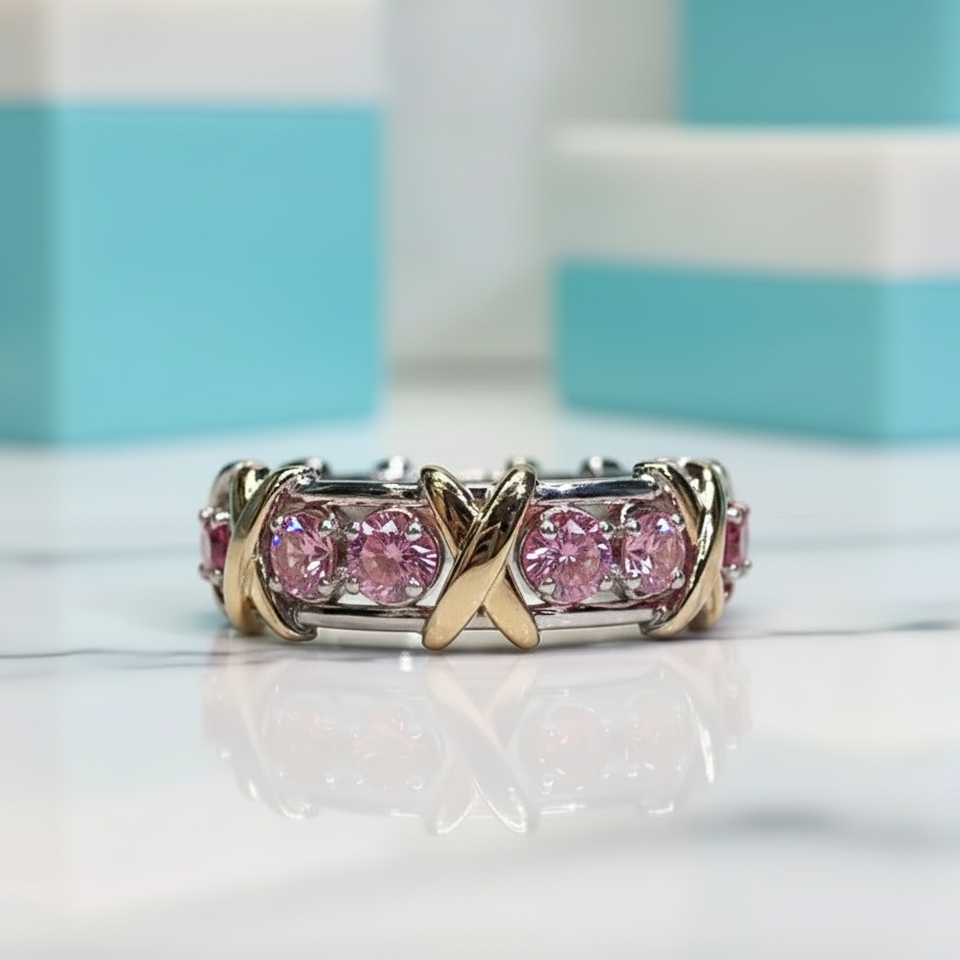 Gold and silver ring with pink gemstones on a reflective surface with a striped background