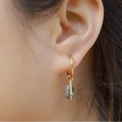 Gold hoop earring with a teardrop-shaped gemstone worn by a person.