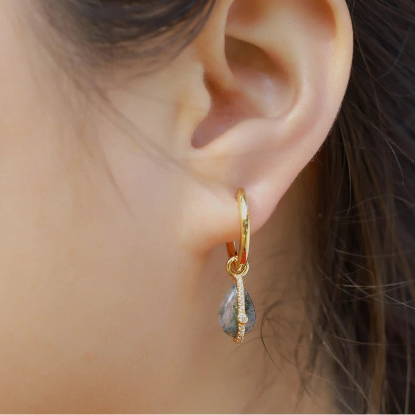 Gold hoop earring with a teardrop-shaped gemstone worn by a person.