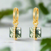 Gold hoop earrings with green gemstones and clear stones on a white background