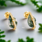 Gold hoop earrings with green gemstones on a white background
