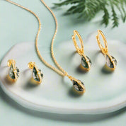 Gold necklace and earrings with green stones on a white background