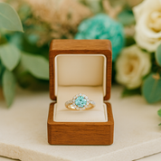 Gold ring with a blue gemstone in a wooden box against a floral background