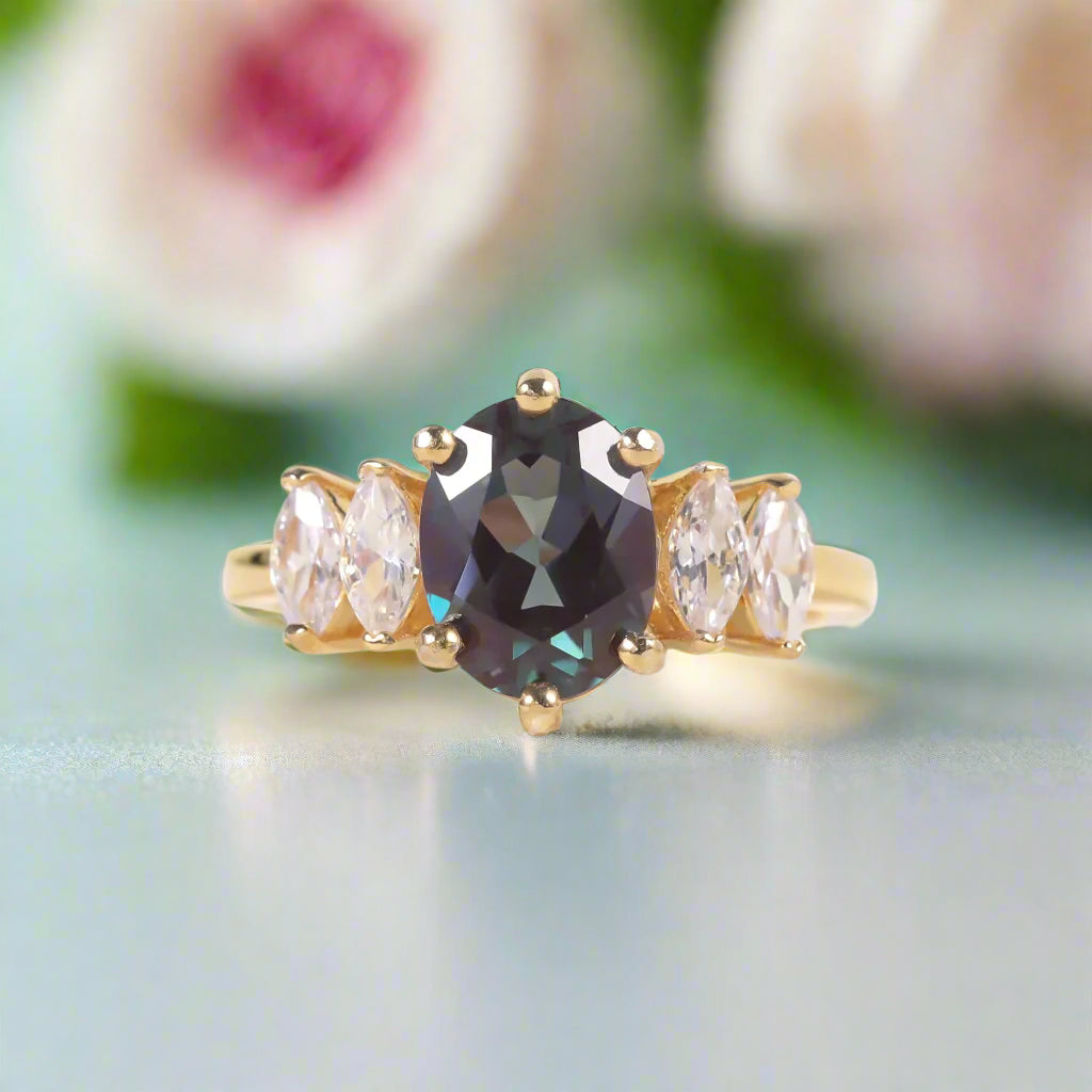 Gold ring with a central dark gemstone and two smaller clear stones on a light background
