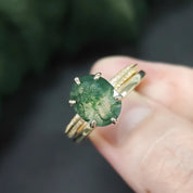 Gold ring with a green gemstone held in a hand against a blurred natural background