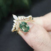 Gold ring with a green gemstone held on a finger against a blurred green background
