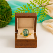 Gold ring with a green gemstone in a wooden box against a natural background