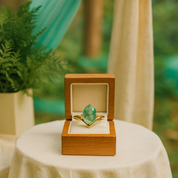 Gold ring with a green gemstone in a wooden box on a table with a blurred natural background