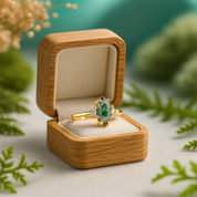 Gold ring with a green gemstone in a wooden box surrounded by greenery
