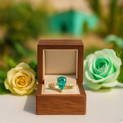 Gold ring with a green gemstone in a wooden box surrounded by roses.