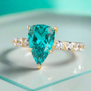 Gold ring with a green gemstone in a wooden box surrounded by roses.