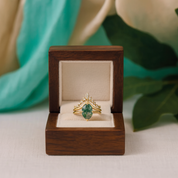Gold ring with a green gemstone in a wooden box with a floral background
