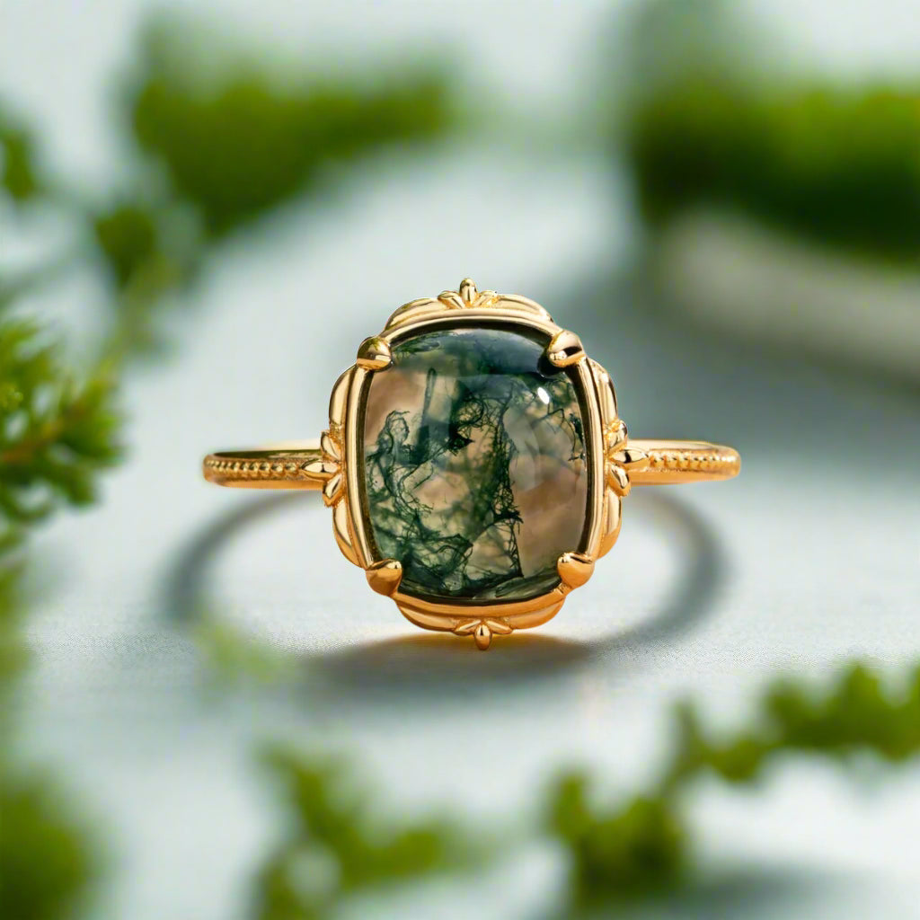 Gold ring with a green stone on a wooden surface with blurred green leaves in the background
