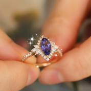 Gold ring with a purple gemstone held between fingers against a blurred background