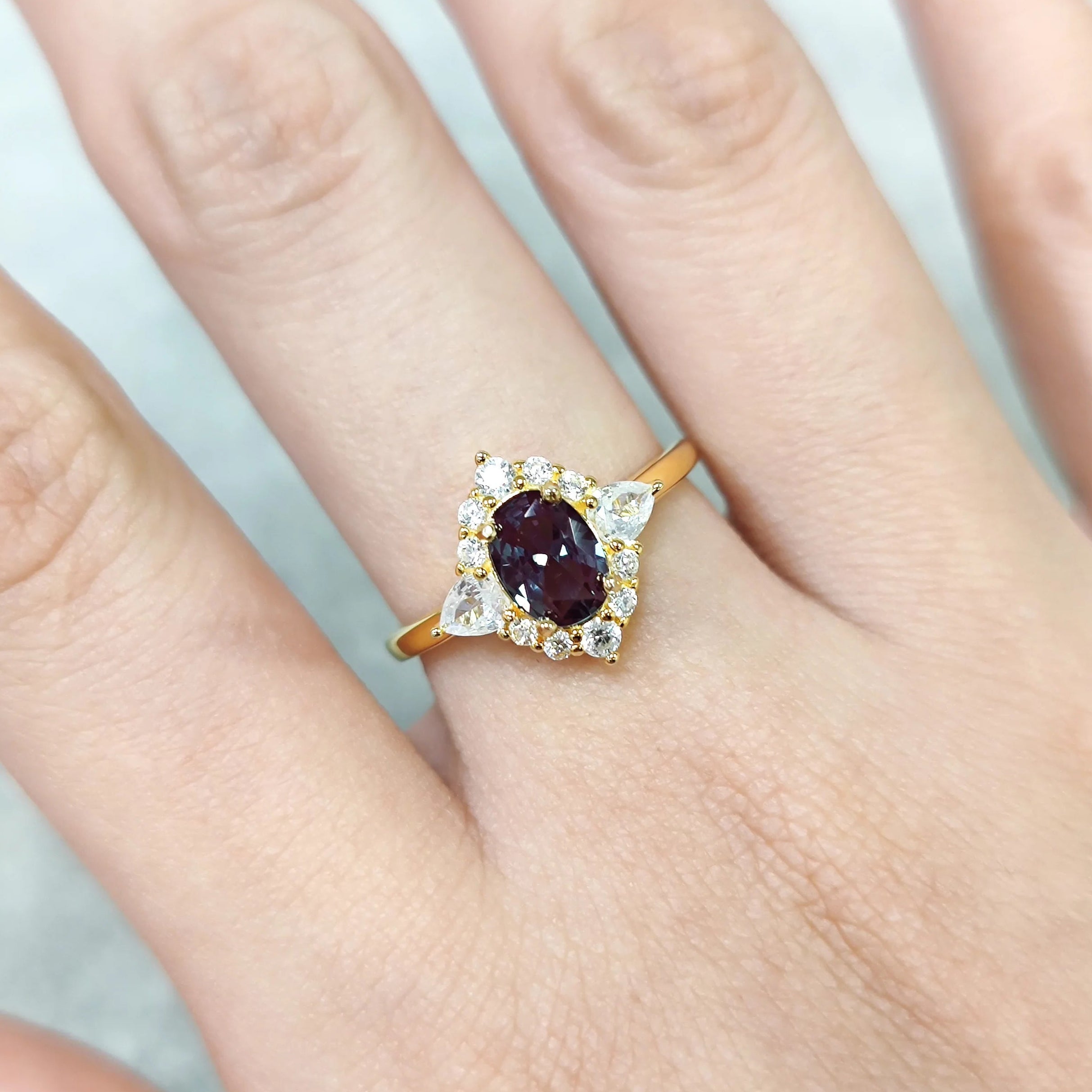 Gold ring with a purple gemstone on a finger against a light background