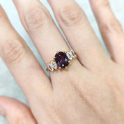 Gold ring with a purple gemstone on a hand against a light background