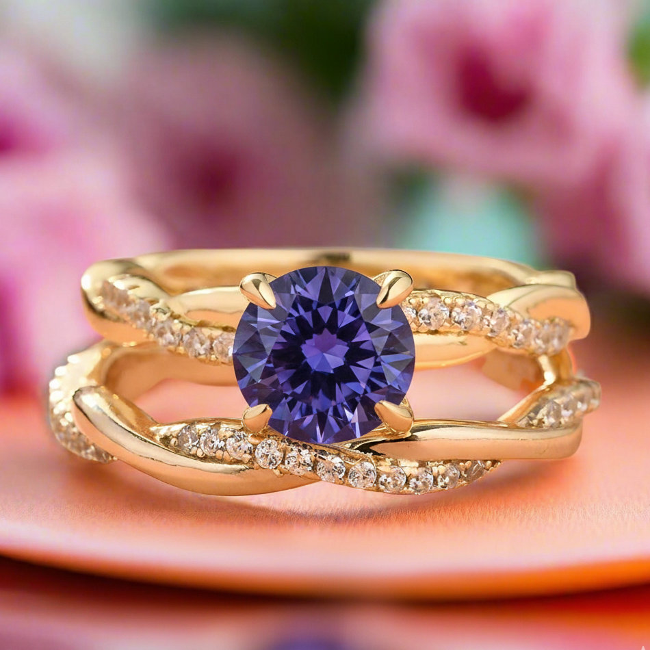 Gold ring with a purple gemstone on an orange surface with pink flowers in the background