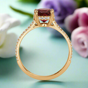 Gold ring with a red gemstone and diamond accents on a white background
