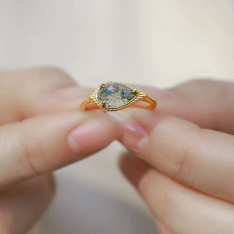 Gold ring with a teardrop-shaped gemstone on a blurred background
