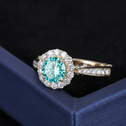 Gold ring with a turquoise gemstone and diamond halo on a dark blue box