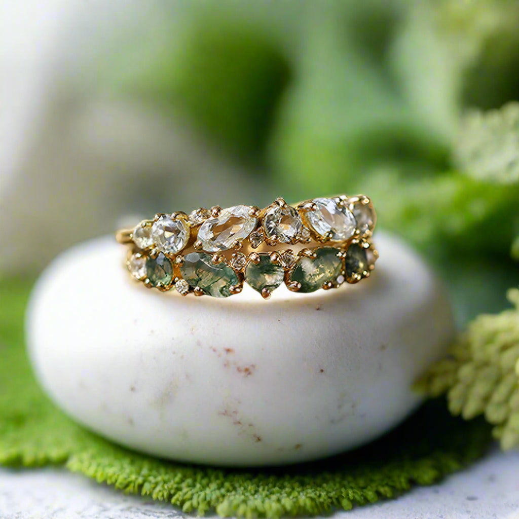 Gold ring with green and clear gemstones on a wooden block