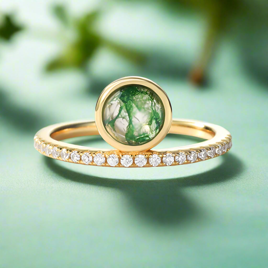 Gold ring with green gemstone and diamond-studded band on a white background